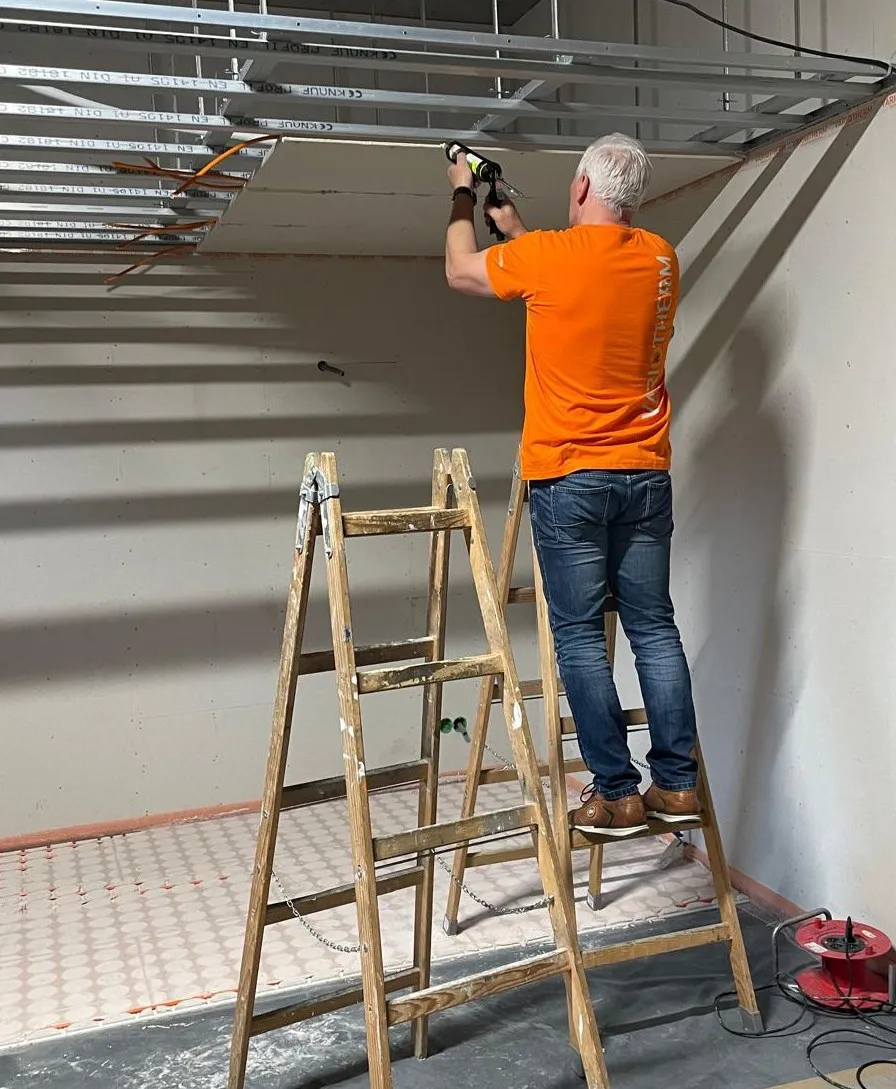 Rolf Lösch montiert auf der Leiter stehend ein Deckenelement
