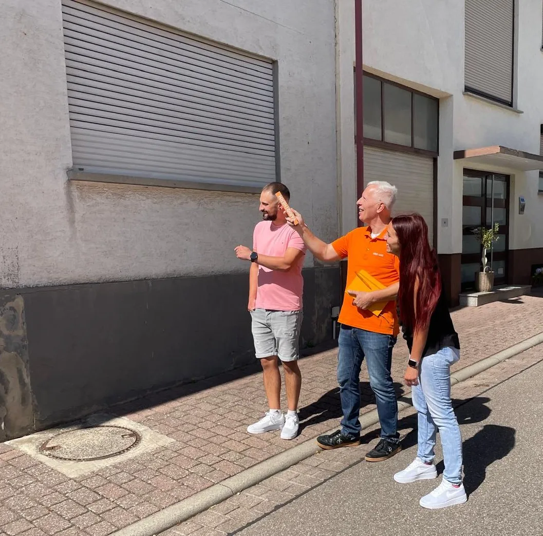 Rolf Lösch geht mit einem Kaufinteressenten-Paar an einem Altbau entlang