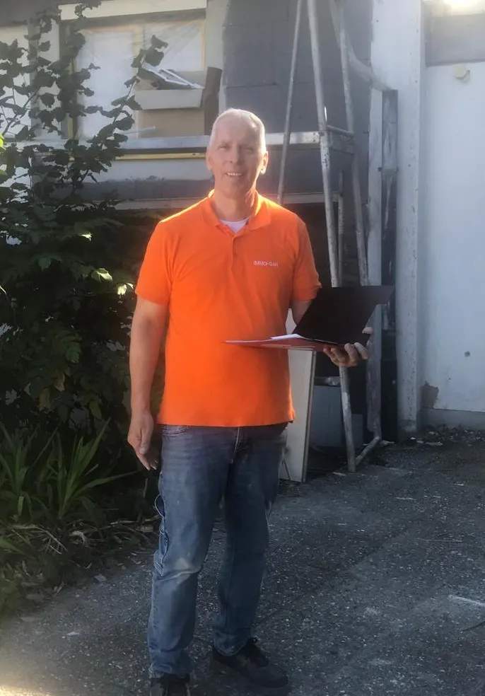Rolf Lösch mit dem Laptop unter dem Arm vor einem Objekt